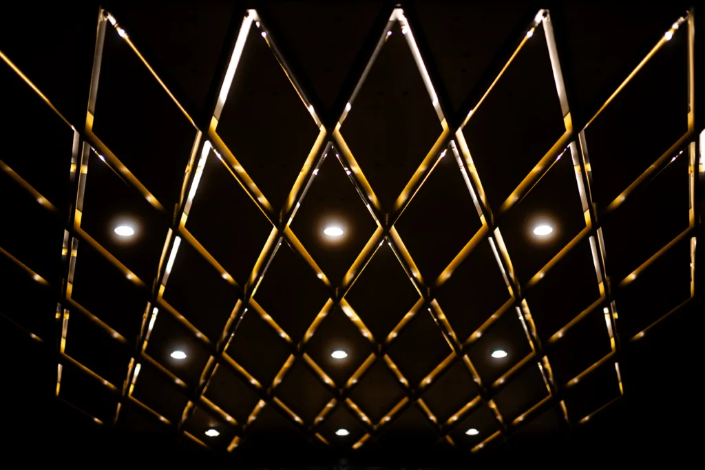 Diamond-patterned metal grid below a ceiling, backlit by warm downlights
