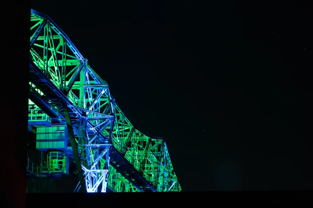 Steel headframe of a former colliery at night, lit in green and blue